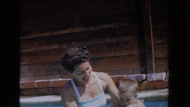 1962: mother dipping her son in and out of the swimming pool. VAN NUYS