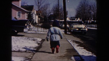 1961: a heavily bundled child outside, walking down a neighborhood sidewalk