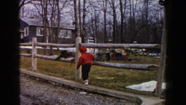 1961: child walking along the timber wood to peek through through the fence.