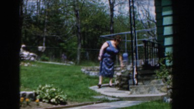 1961: an old lady watering the plants at her garden finds her husband and talks