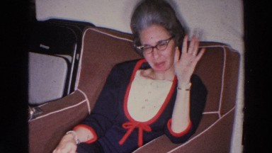 1966: an older woman in a bouffant hairstyle and navy blue dress greeting the camera
