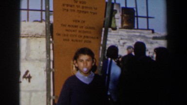 1960: person blowing a bubble in front of a sign next to some other people