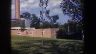 1960: a large brick building with a smoke stack against a beautiful cloudy sky
