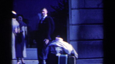 1963: a gentleman in formal suit standing near to some luggage