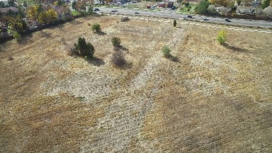 aerial panning view of field with trees adjacent to road with moderate traffic