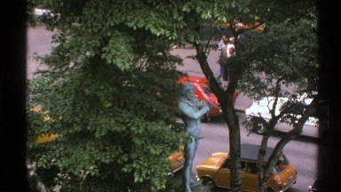 1976: Statue of Man Playing Violin in Front of Tree and Street