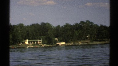 1976: view of large house on the coast as seen from a passing marine vessel.