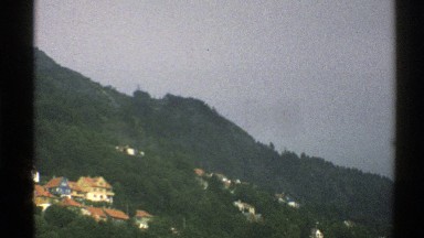 1976: a tranquil view of a town in the mountains, followed by a parked airplane