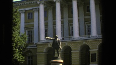 1975: structure of a person that is pointing, positioned in front of building