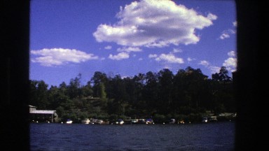 1975: A serene lakeside town scene in Stockholm with blue water and greenery