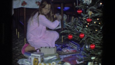 1971: girl with pink pajamas unpacking gifts under christmas tree on xmas
