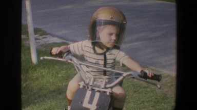 1973: a young boy sitting on a bike wearing a helmet with faceplate and number