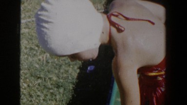 1953: little girl in her swimsuit and cap, playing in the yard sprinklers, jumps
