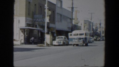 1951: a street with several parked cars along the curb with buses and cars