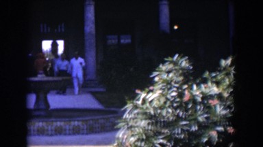 1951: People Walking Out From a Fancy Hotel and a Lady Sitting in Front