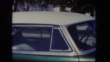 1954: a person is sitting inside a green and white colored sedan parked
