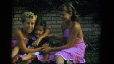 1954: 3 little girls, 2 in matching pink halter skirt outfits, sit and wave