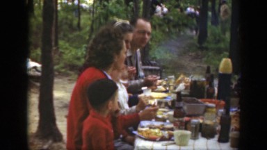 1949: a large family meal at a picnic table at a campground in the woods