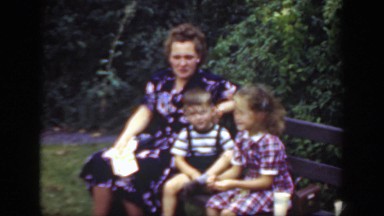 1948: mother and her two children sitting on a park bench on a windy day.
