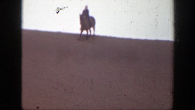 1939: a man slowly going down a sand dune on a horse and followed by a woman