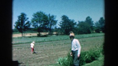 1957: three individuals outside on farm land walking and harvesting the crops