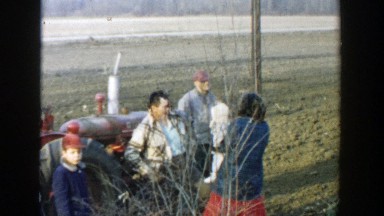 1958: Mom Hands Son to Dad as Three Boys Pose with Him Around Tractor