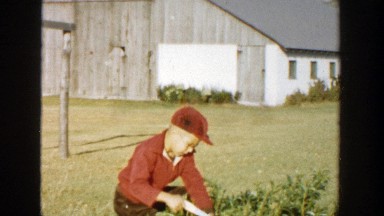 1958: child in a hat outside using a tool to remove some branches of a plant
