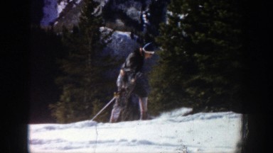 1961: man in heavy coat walking up snowy mountain with his skis on ASPEN