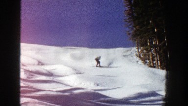 1961: an amateur male skier slowly skis down a hill and passes a group of trees