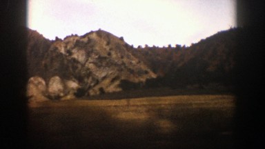 1961: a moving vehicle beside of a mountain,fields and trees with a beautiful