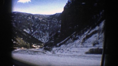1961: a car makes a scenic drive through the snowy mountains. ASPEN COLORADO