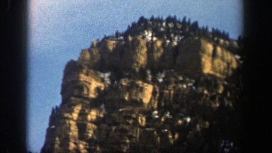 1961: boulder-covered mountain peak with forest and pockets of snow under a blue