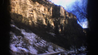 1961: driving on a two lane road through a canyon with snow of the ground and
