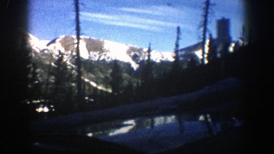 1961: driving past big pine trees and large snow capped mountains. ASPEN