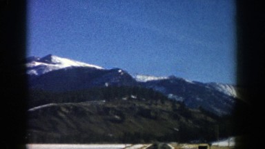 1961: a mountain range seen from a long straight road with snow on the ground