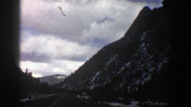 1961: the view of a mountain from the road below as travelers drive during a