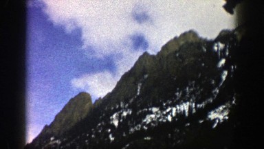 1961: Snow Clings to the Side of a Forested Mountain Slope on a Partial Cloudy Day