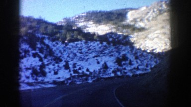 1961: a car drives down a rounding highway surrounded by mountains. ASPEN
