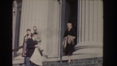 1960: party of people carrying assorted coats and purses, walking down steps
