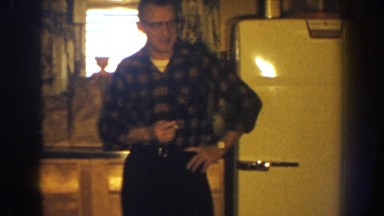 1959: man in patterned shirt talks in a kitchen area while holding a cigarette.