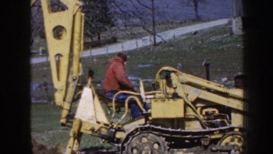 1958: construction vehicle driver operates backhoe on an open, rural field