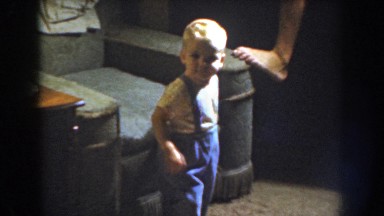 1959: a male toddler wearing overalls and a tee shirt walking towards the person