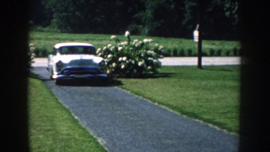 1959: Plymouth Driving Up a Narrow Driveway Sandwiched Between Green Manicured Lawns