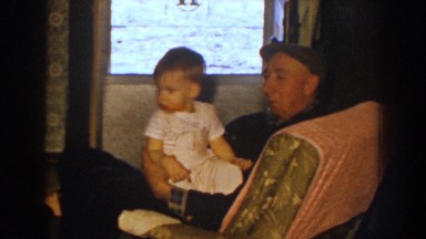 1959: a home scene of a man rocking a baby girl and a woman fixing another