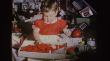 1955: a small girl in a red dress opens presents and holds money in her hand.