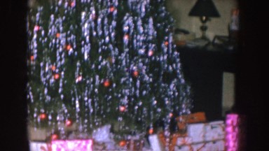 1955: christmas tree loaded with tinsel in a living room with many presents