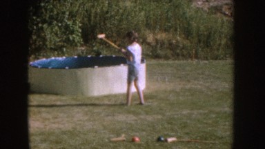 1955: woman hits ball with croquet mallet as girl and other family stand or sit