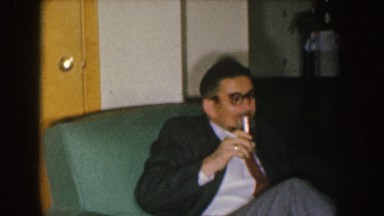 1955: a man wearing a suit and tie drinks and smokes while talking to a couple