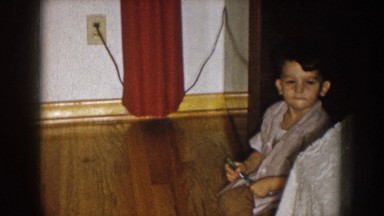 1957: a small child sitting at the foot of a bed holding something. NEBRASKA
