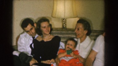 1957: family sitting on a couch next to christmas presents and talking, and box